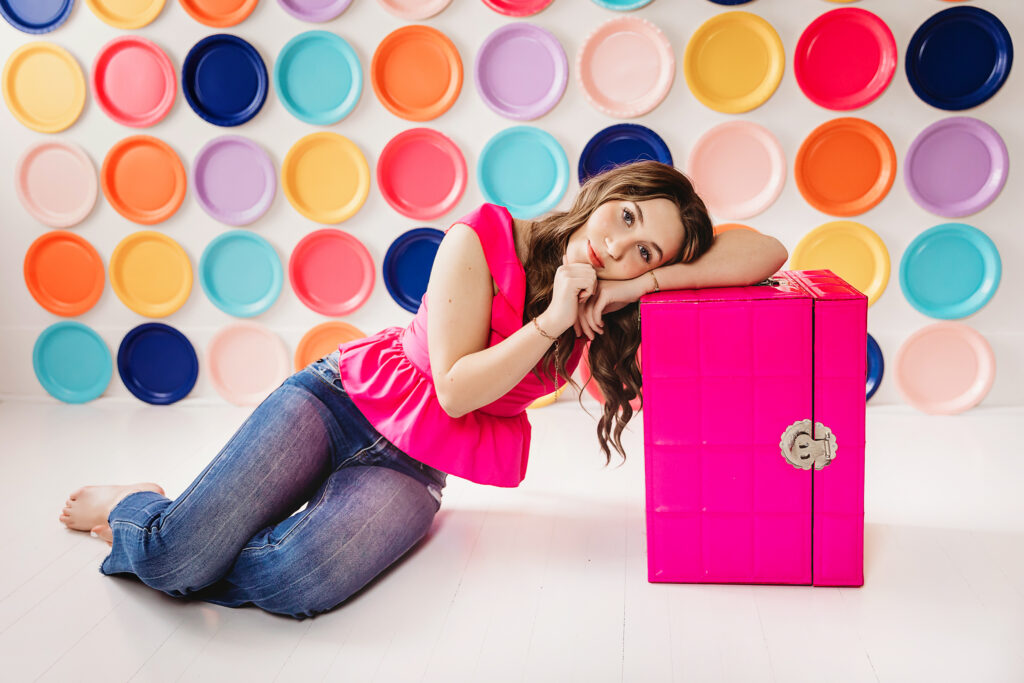 Teen girl resting her head on a pink trunk, colorful plates in the background.