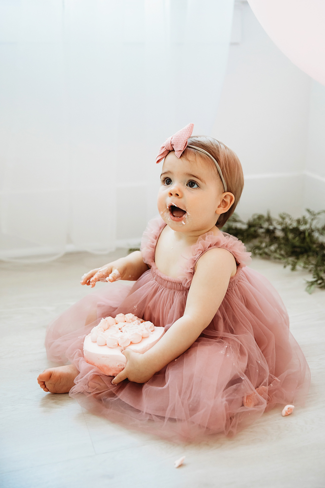 Grace with frosting on her lips and mouth wide open, holding the cake close to her chest in a pink tulle dress at Reflection Images by Tracy Rowell in Florence SC
