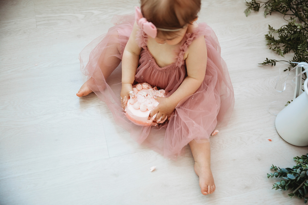 Grace smashing the cake with both hands, frosting everywhere, wearing a ruffled pink dress and headband at Reflection Images by Tracy Rowell in Florence SC