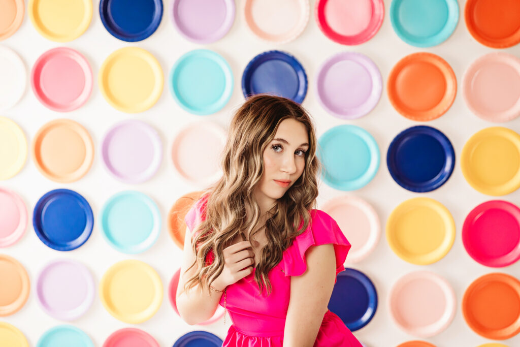Close-up of teen girl smiling slightly with soft curls, vibrant wall behind her.