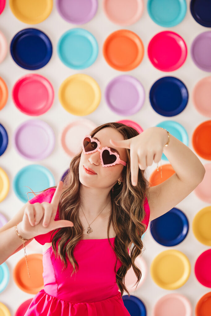 Teen girl framing her face with hands while wearing pink heart glasses.
