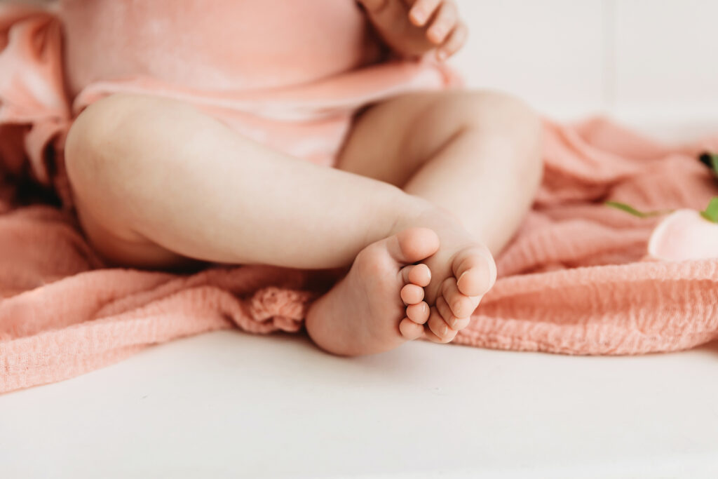 Close-up of Sullivans tiny toes resting on a blush gauze blanket during her first birthday session at Reflection Images by Tracy Rowell in Florence SC.