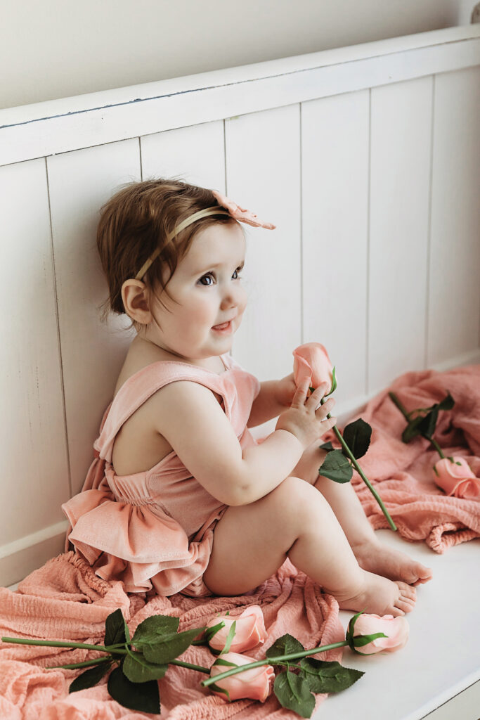 Side portrait of Sullivan holding roses while sitting on a white bench with a peach blanket at Reflection Images by Tracy Rowell in Florence SC.