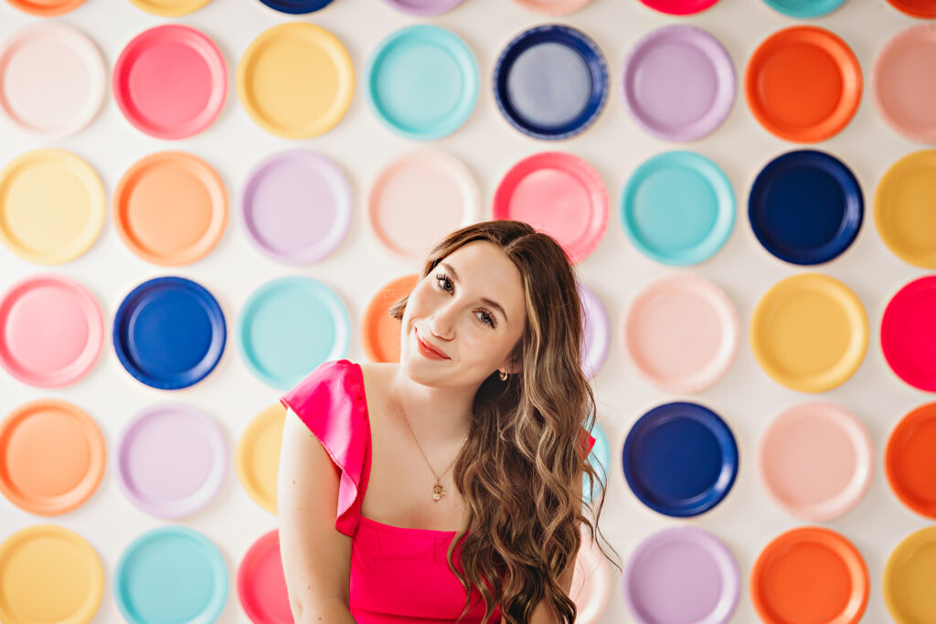 Young woman smiling with curled hair in front of rainbow plate wall, bright casual look