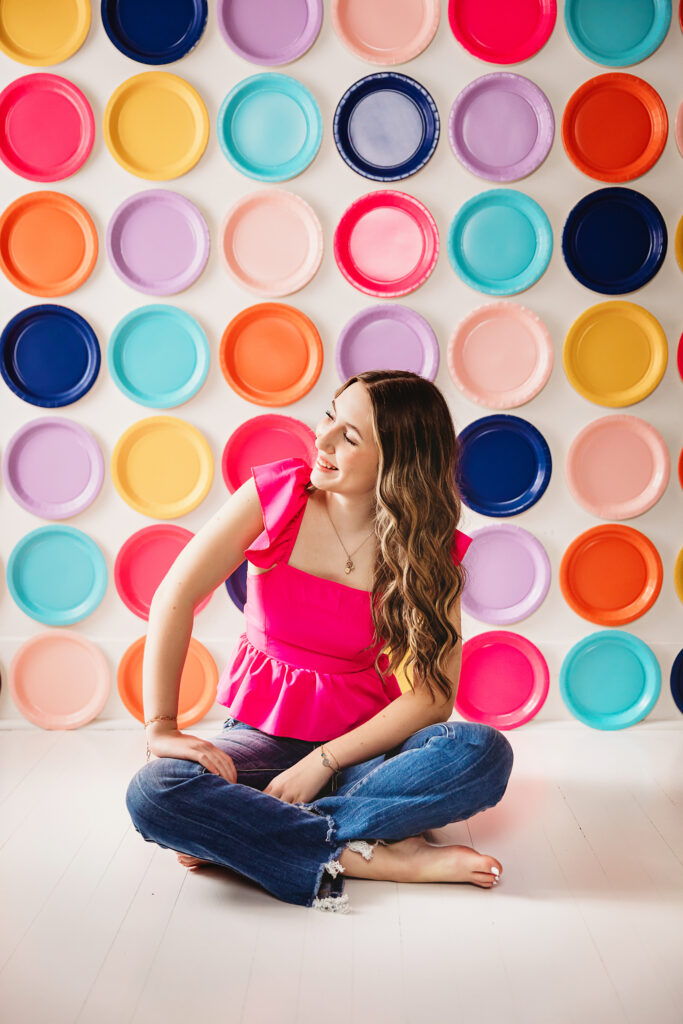 Seated cross-legged, woman laughing and looking sideways against colorful paper plate wall