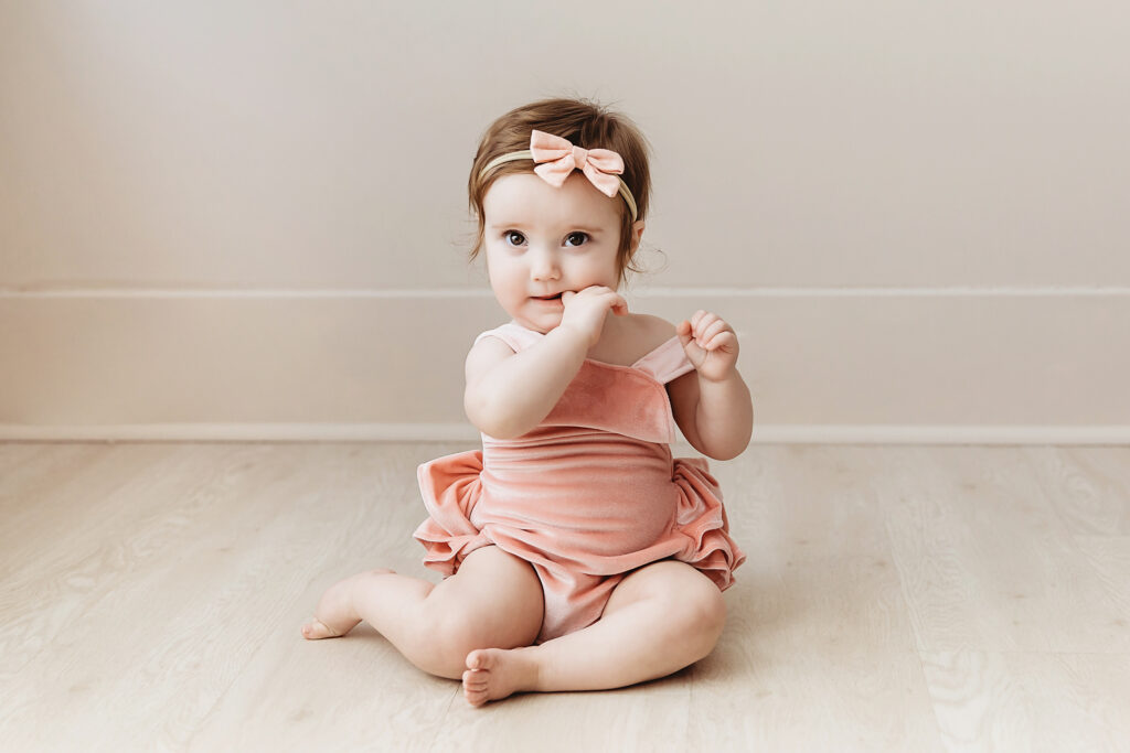 Sullivan seated on a light wooden floor wearing a blush velvet romper and headband, with soft natural light at Reflection Images by Tracy Rowell in Florence SC.