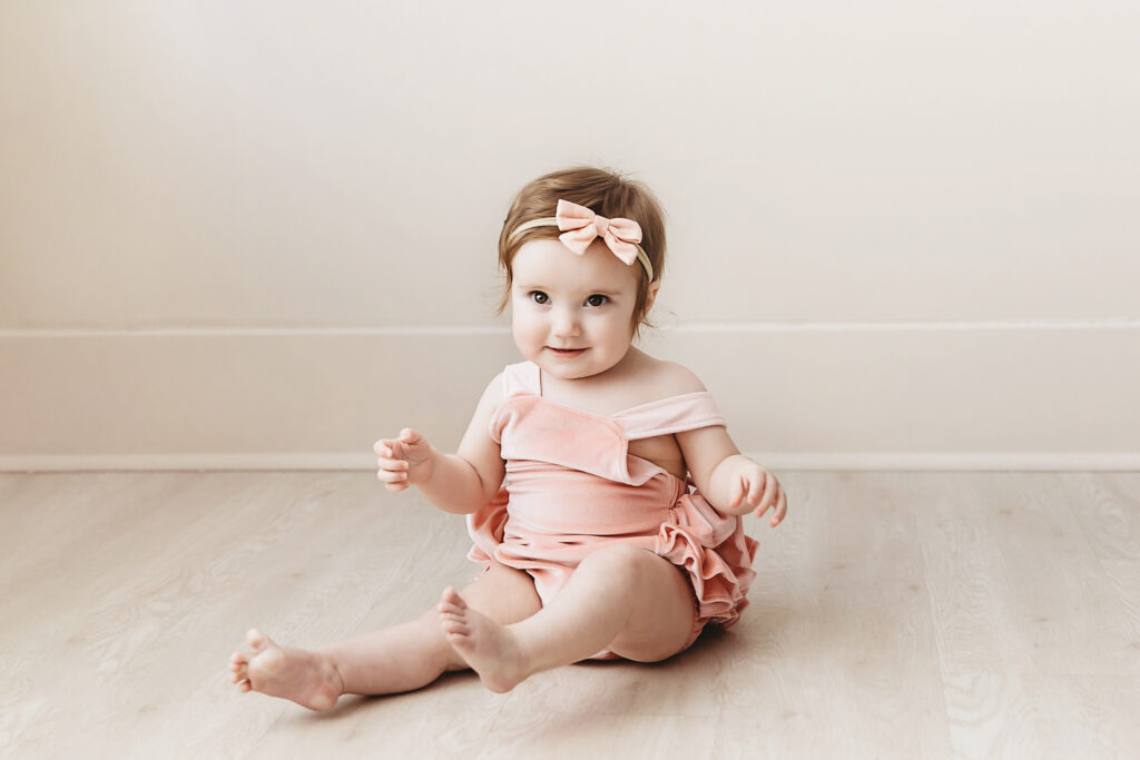 Happy moment of Sullivan playing on the studio floor in a ruffled blush romper and bow headband at Reflection Images by Tracy Rowell in Florence SC.