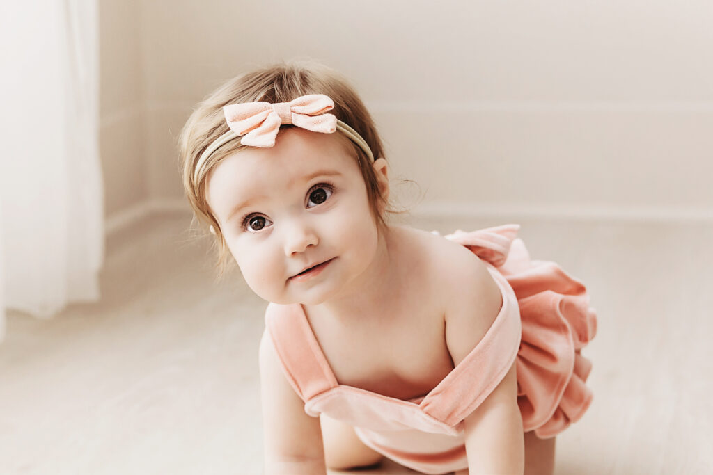 Crawling close-up of Sullivans face with big gorgeous eyes and a blush romper under soft studio lighting at Reflection Images by Tracy Rowell in Florence SC.