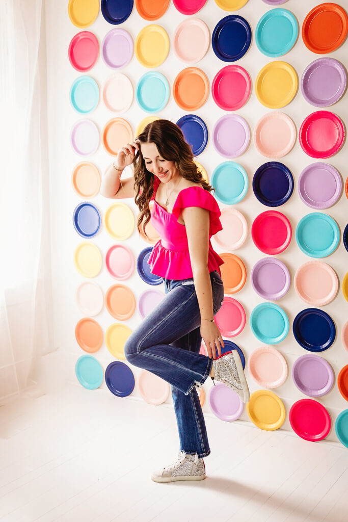 Standing with one foot up and glitter shoes, woman in vibrant pink and distressed jeans
