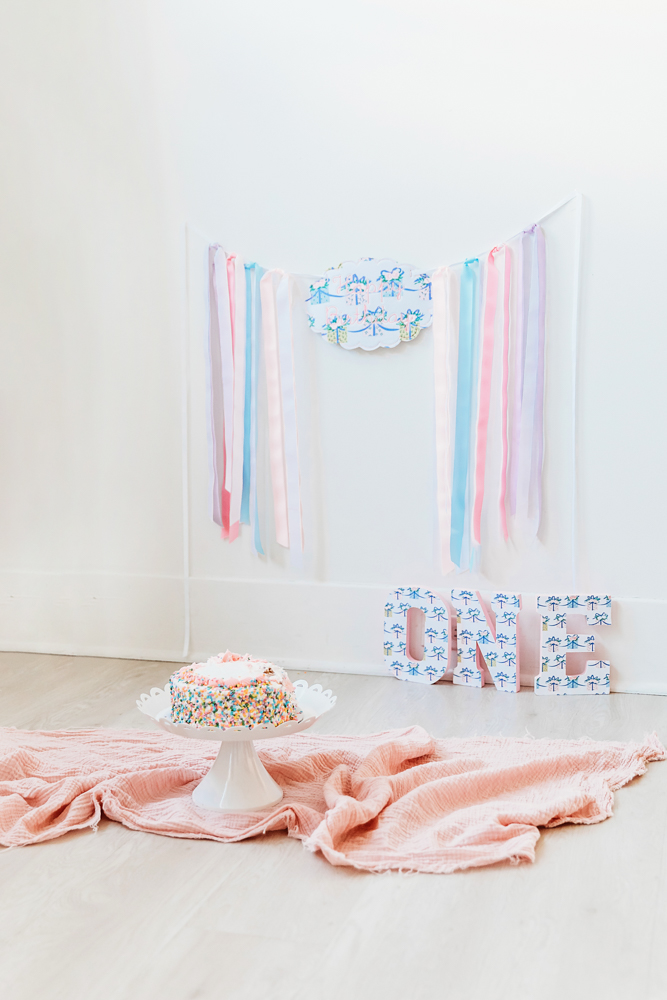 Sprinkle cake on white stand with pink blanket and ONE letters, pastel ribbon backdrop birthday setup at Reflection Images by Tracy Rowell in Florence SC