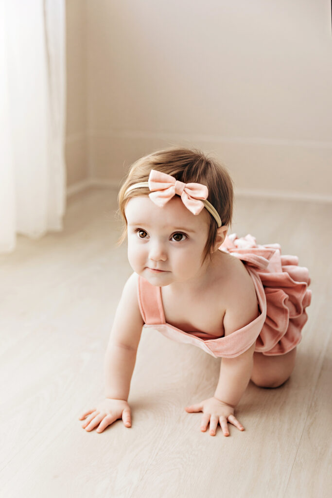 Vertical image of Sullivan mid-crawl in soft morning light with peach tones and blush outfit at Reflection Images by Tracy Rowell in Florence SC.