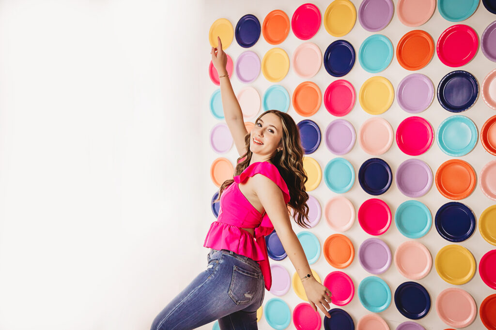 Double arm point pose with joyful expression, colorful plates on wall background