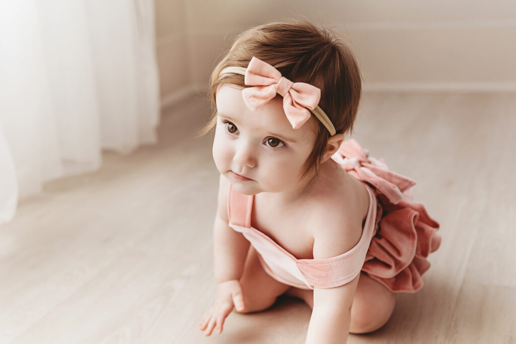 Curious expression from Sullivan crawling in studio light, wearing a ruffled romper and peach bow at Reflection Images by Tracy Rowell in Florence SC.