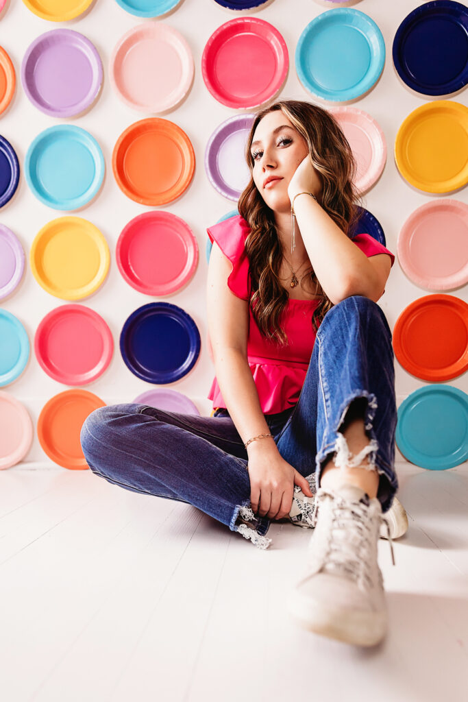 Teen girl glowing under soft white light while laying on floor in front of colorful circle backdrop, denim jeans and pink blouse at Reflection Images by Tracy Rowell in Florence SC