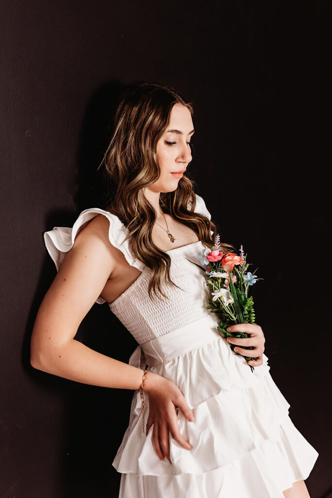 Teen girl standing against black wall in white dress with flowers at Reflection Images by Tracy Rowell in Florence SC