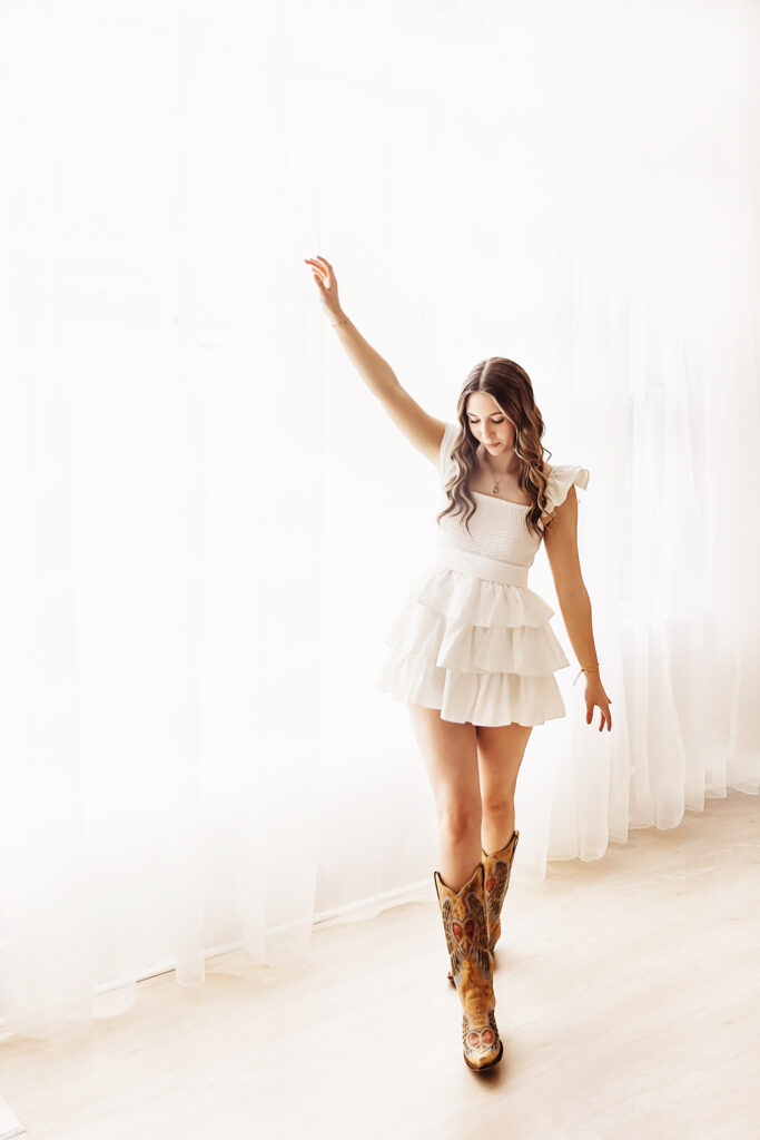 Teen girl standing against window wall in white dress with arm up at Reflection Images by Tracy Rowell in Florence SC