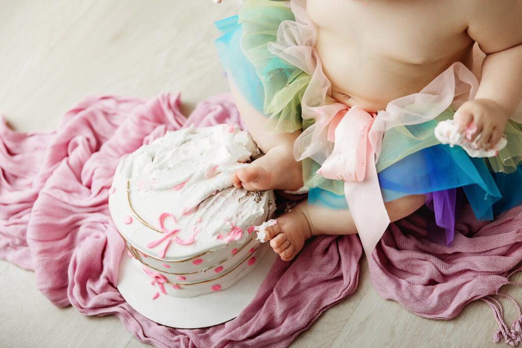 Sullivan gazing up during her cake smash with pastel banners and cake nearby on a pink blanket at Reflection Images by Tracy Rowell in Florence SC.