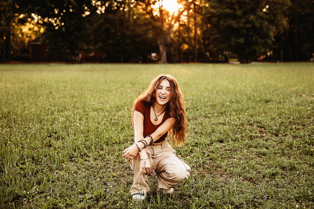 Eve kneels in the field, laughing with joy, the evening sunlight glowing behind her.