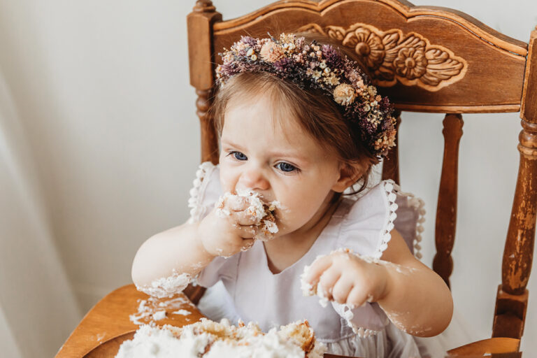 Close-up of toddler girl making a mess as she digs into her birthday cake with her hands and mouth.