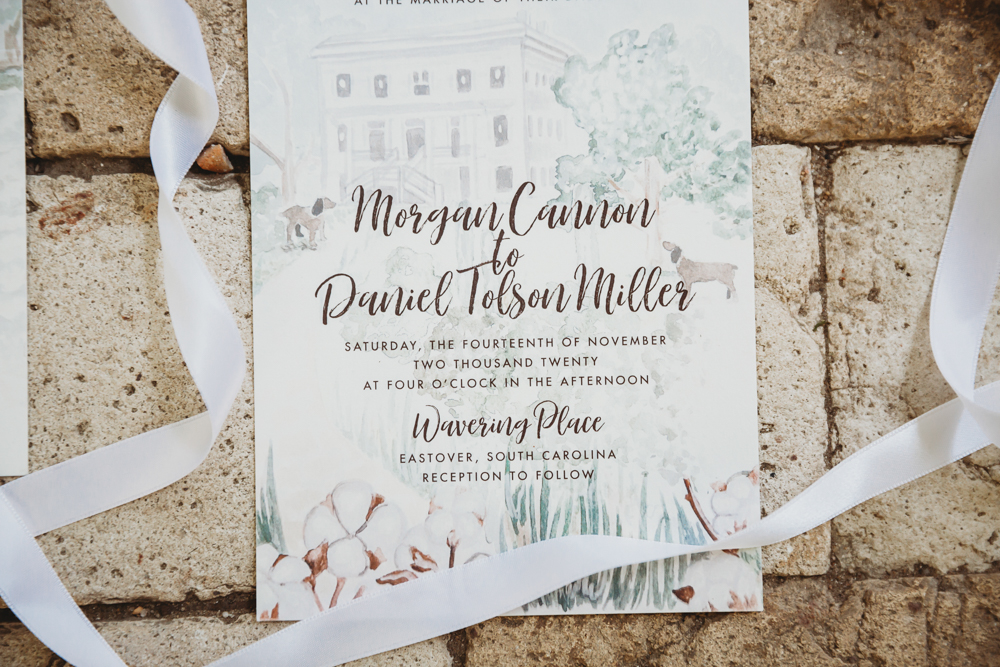 Elegant watercolor wedding invitation for Morgan and Daniel styled on rustic brick with flowing white ribbon details.