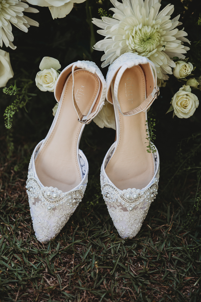 White bridal heels with pearl beading styled among ivory blooms and greenery on natural grass.