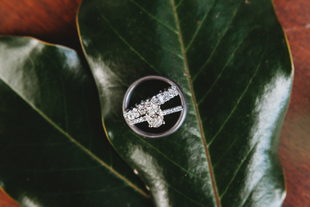 Diamond engagement ring and wedding band on magnolia leaves, reflecting light and texture at Wavering Place.
