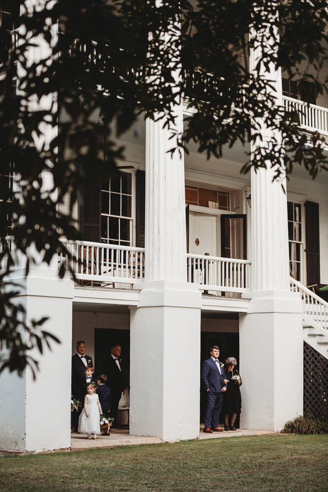 Groom and wedding party wait under grand white columns of the Wavering Place porch before the ceremony begins