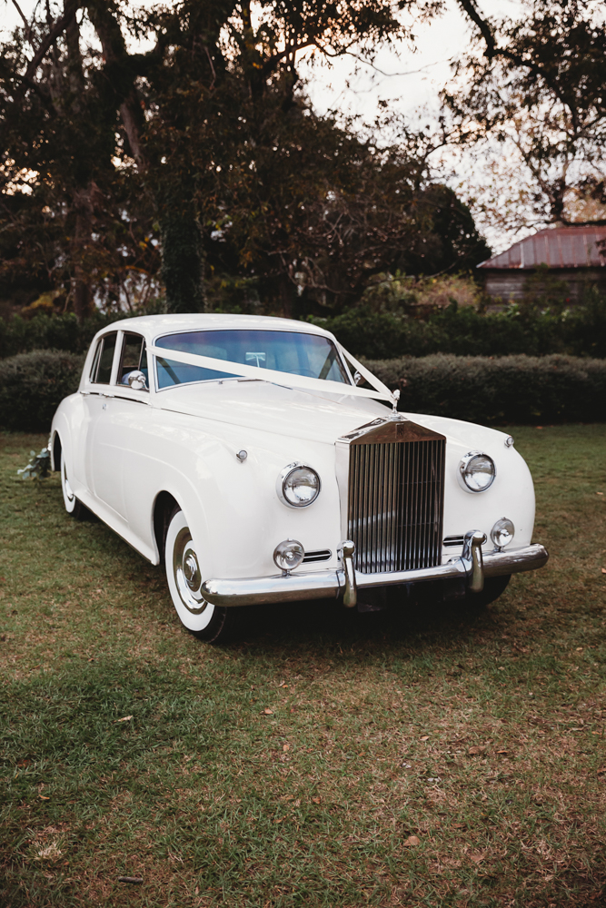 Classic white Rolls Royce with wedding ribbon parked on grass, ready for the couple’s getaway from Wavering Place
