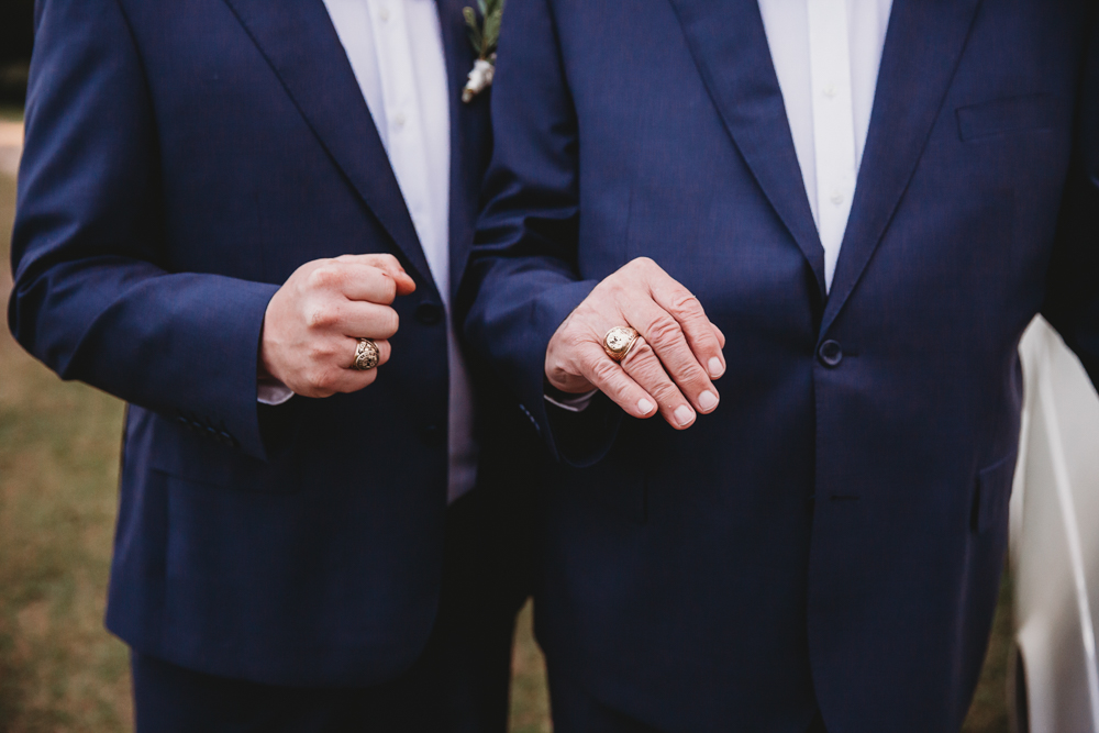Close-up of matching gold rings on the groom and father’s hands, both in deep blue suits, taken by Reflection Images by Tracy Rowell