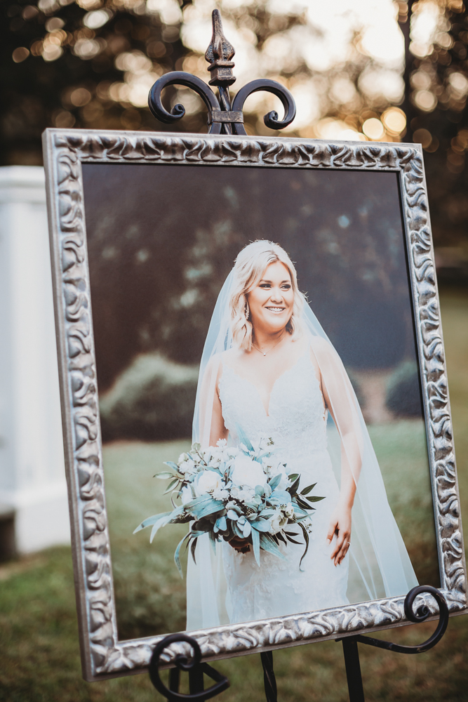 Elegant framed bridal portrait featuring bride in lace gown holding white bouquet, displayed on ornate metal easel at Wavering Place, by Reflection Images by Tracy Rowell in Florence SC.