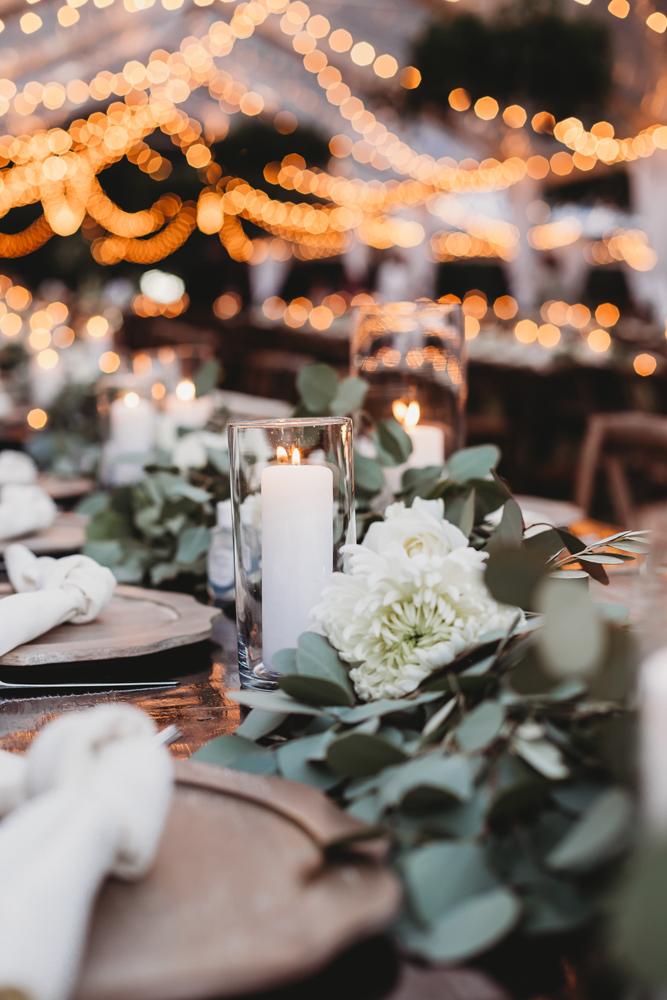 Elegant reception tablescape with candles, eucalyptus garland, and glowing bokeh lights strung overhead at Wavering Place, captured by Reflection Images by Tracy Rowell in Florence SC.