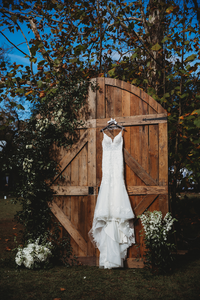 Full-length wedding dress hanging on large wooden doors surrounded by greenery at Wavering Place.