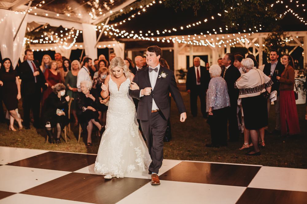 Bride and groom’s first dance on a black and white checkered dance floor under string lights at Wavering Place, with guests gathered close, by Reflection Images by Tracy Rowell in Florence SC.
