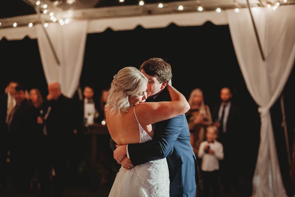 Emotional first dance moment as the bride and groom embrace under string lights during their Wavering Place reception, captured by Reflection Images by Tracy Rowell in Florence SC.
