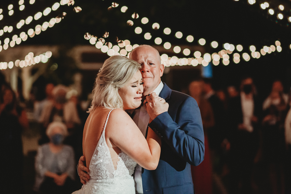 Bride shares a tearful and heartfelt dance with her father beneath glowing bistro lights at Wavering Place, photographed by Reflection Images by Tracy Rowell in Florence SC.