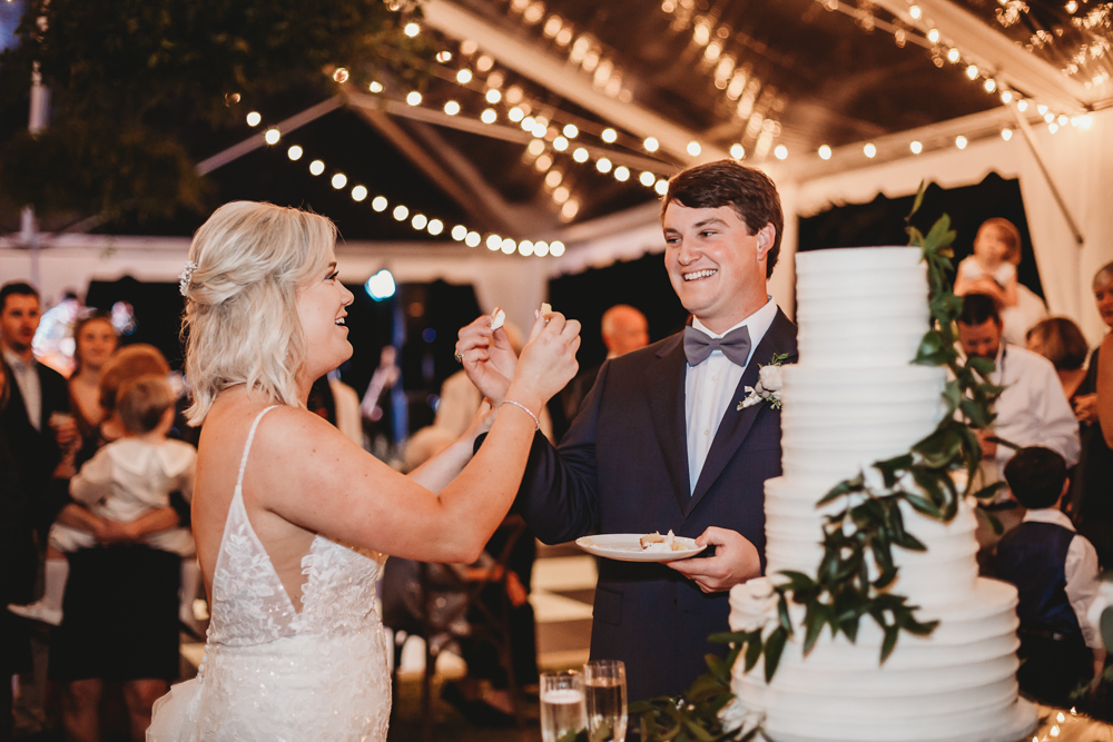 Bride and groom smiling as they prepare to feed each other cake during the reception at Wavering Place, captured by Reflection Images by Tracy Rowell in Florence SC.