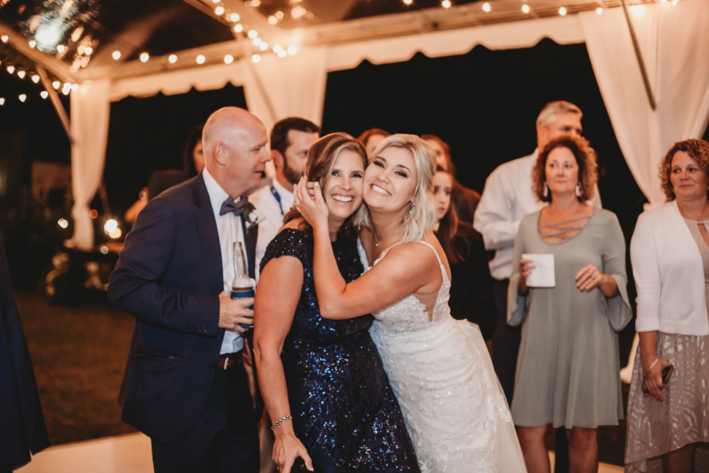 Bride Morgan smiling brightly as she hugs a mom in a sequined navy gown during the lively reception celebration at Wavering Place.