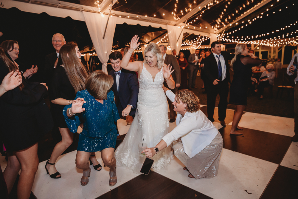 Bride Morgan surrounded by guests of all ages dancing enthusiastically under the tent filled with string lights at Wavering Place.