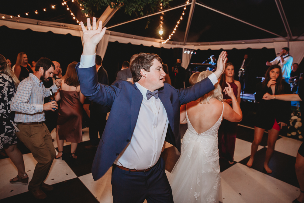 Groom Daniel with arms raised in celebration while dancing with bride Morgan and guests during the fun-filled reception at Wavering Place.
