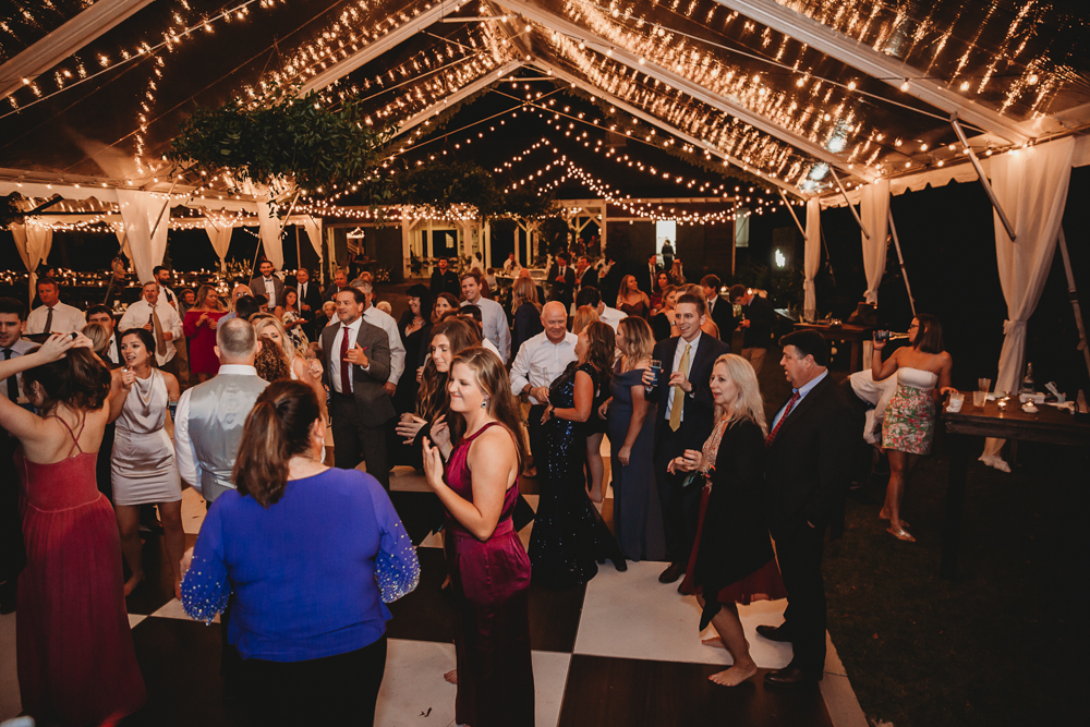 A packed dance floor under a beautifully lit tent, with guests of all ages dancing, laughing, and enjoying the vibrant celebration.