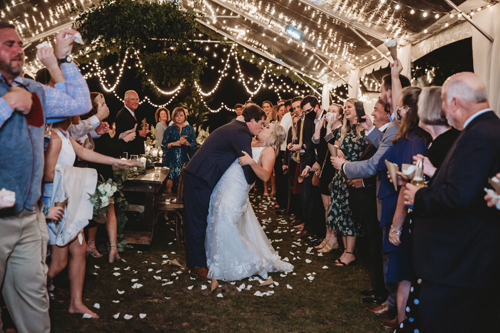 Under a sparkling canopy of lights, the couple shares a dramatic kiss surrounded by cheering guests holding flower petals in celebration of their exit.