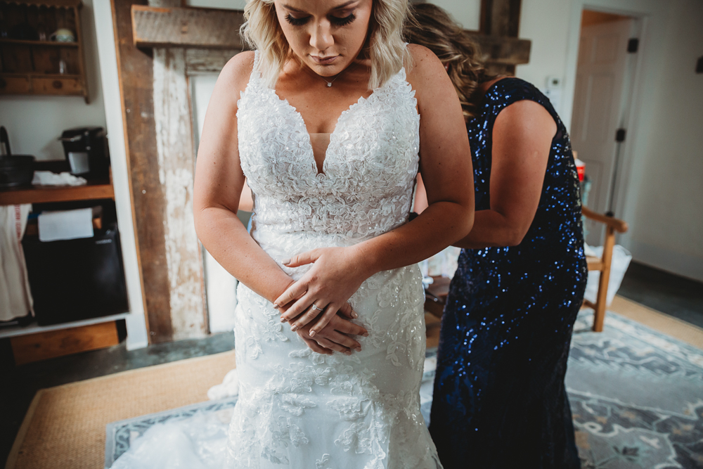 Close-up of bride in lace gown with hands folded, a quiet moment in rustic prep space with wooden accents.