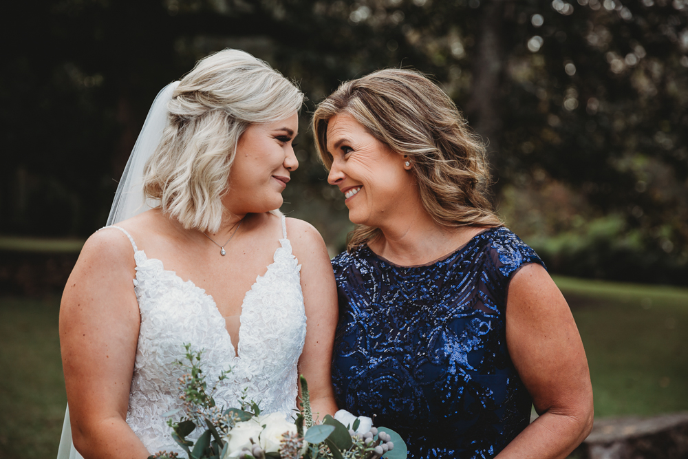 Warm close-up of bride and mother exchanging smiles with deep blue sequined gown and bridal bouquet.