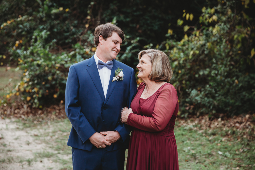 The groom and his mother share a warm moment smiling side-by-side outdoors under soft natural light at Wavering Place in Eastover SC.