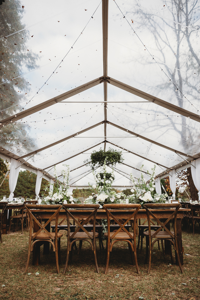 Clear-top tent reception at Wavering Place with rustic farm tables and white florals under greenery chandeliers