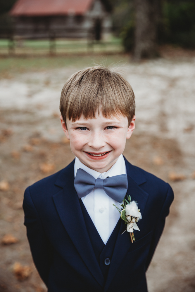 Smiling ring bearer in navy suit and bow tie posing outdoors at Wavering Place