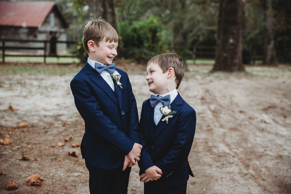Two young ring bearers in navy suits share a joyful moment outside at Wavering Place