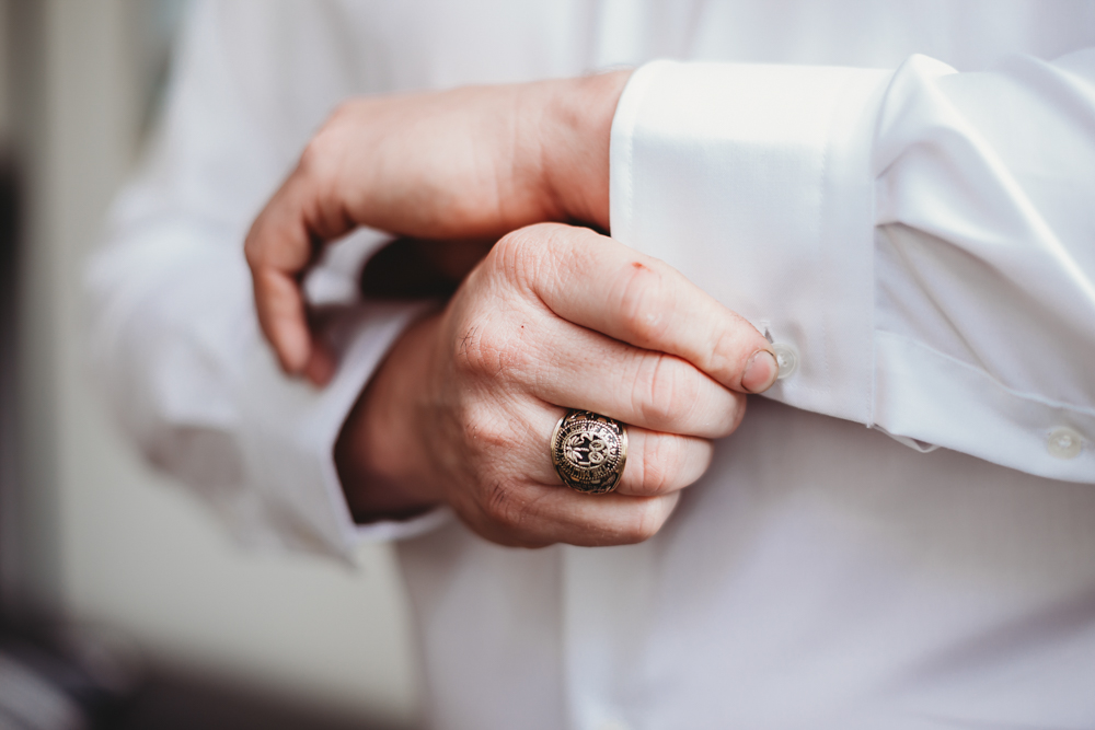 Close-up shot of groom fastening his cufflinks, showcasing a detailed ring on his finger