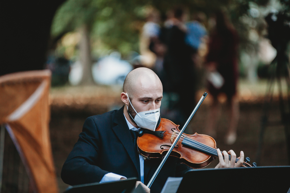 A masked violinist in a dark suit performs during the outdoor wedding ceremony at Wavering Place.