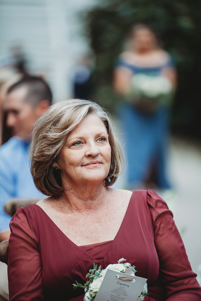 The mother of the groom sits smiling and composed in a maroon dress while watching the ceremony unfold.